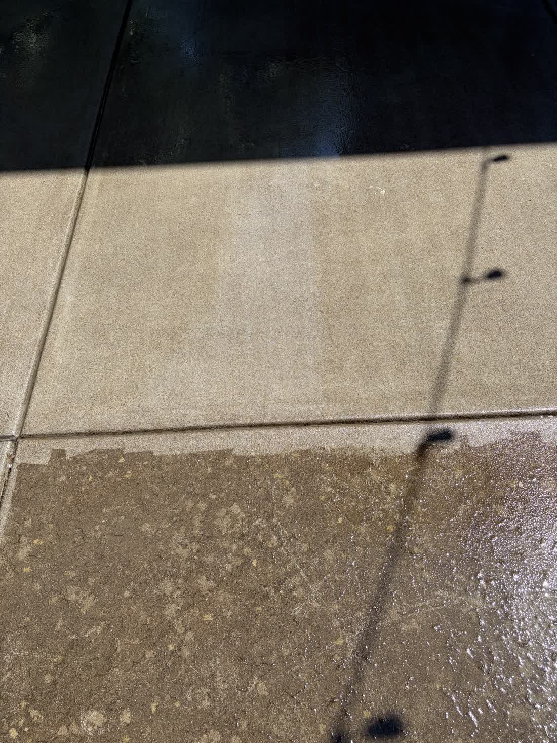 Concrete slab photographed part way through a pressure wash, clean surface beside untouched buildup